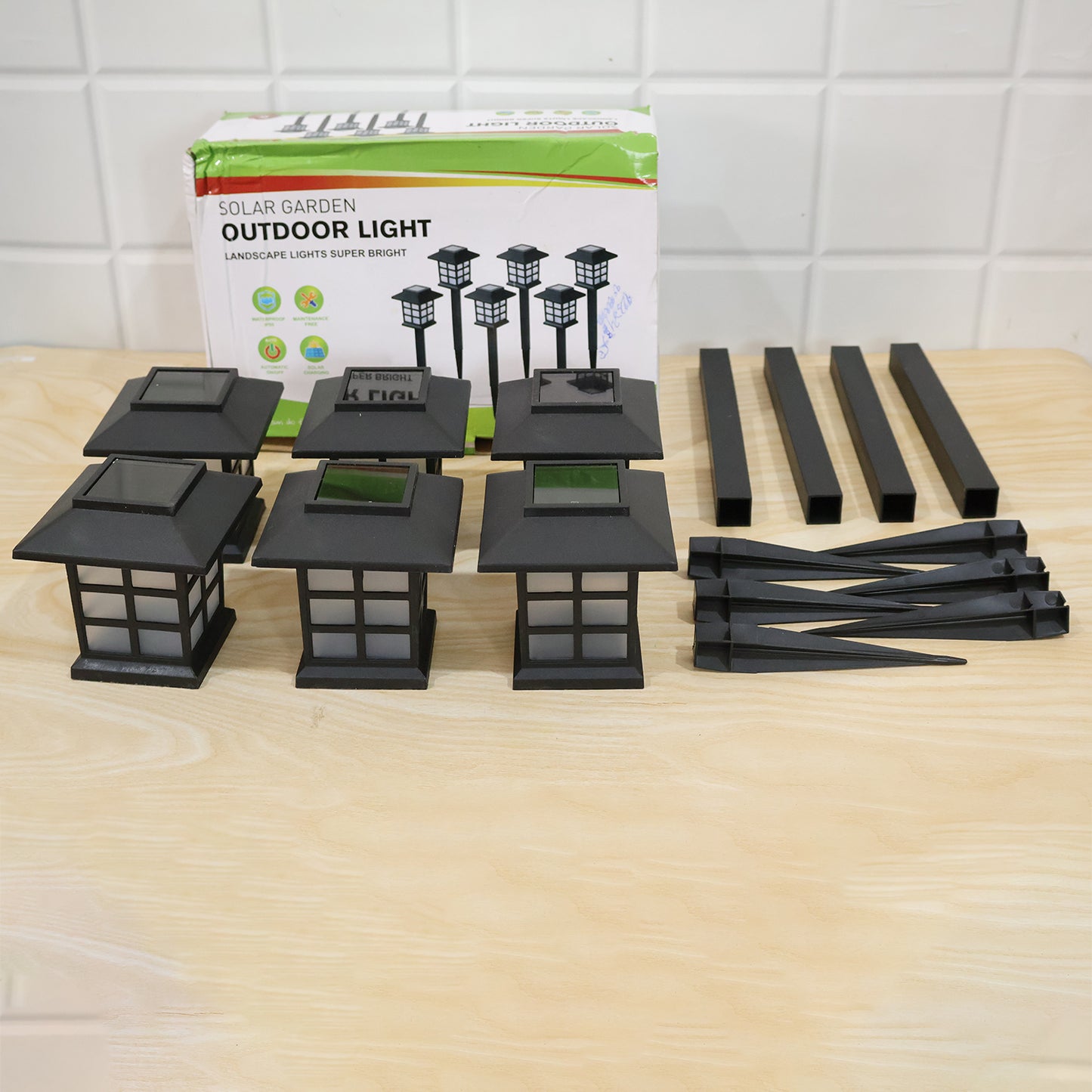 The components of six black solar garden lights are displayed on a wooden surface next to their product box.