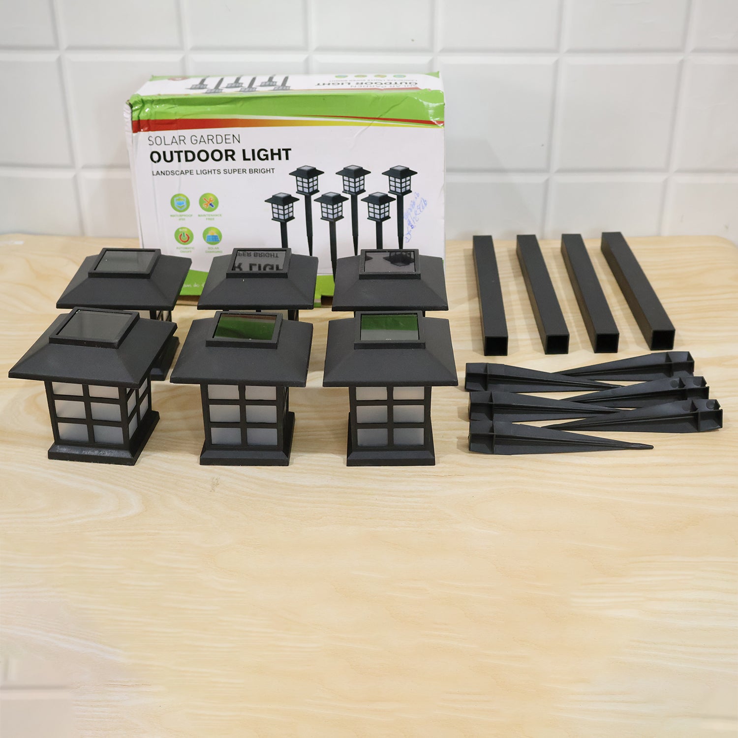 The components of six black solar garden lights are displayed on a wooden surface next to their product box.