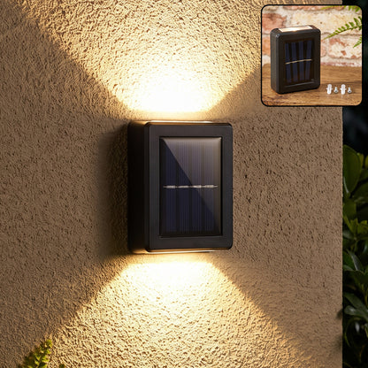 A black solar LED wall light illuminates a textured beige wall with warm light beams pointing up and down, with a smaller