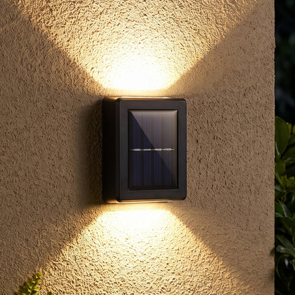 A black solar LED wall light illuminates a textured beige wall with warm light beams pointing up and down, with green