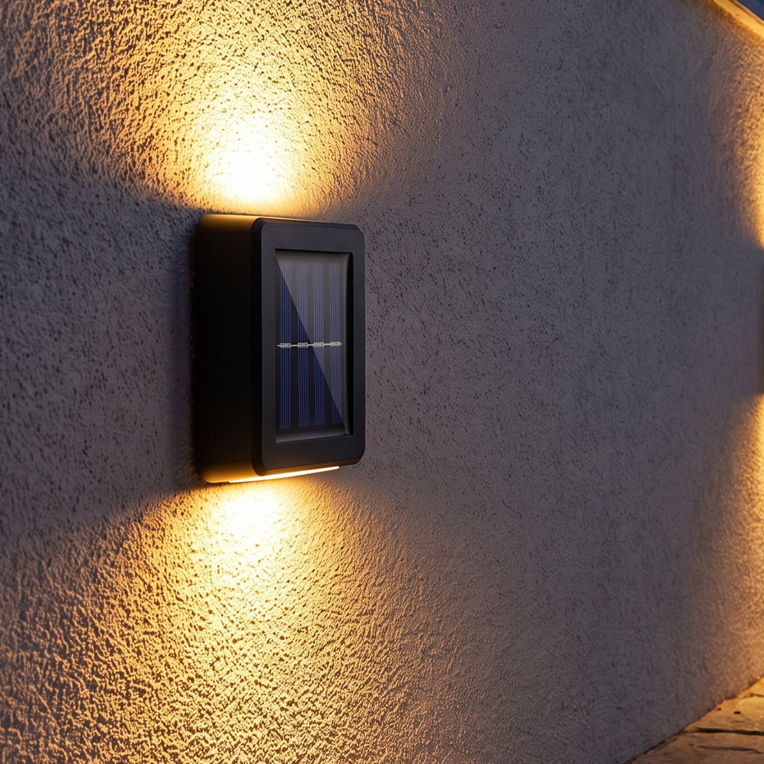 Two black solar LED wall lights illuminate a grey textured wall with warm light beams pointing up and down in an outdoor