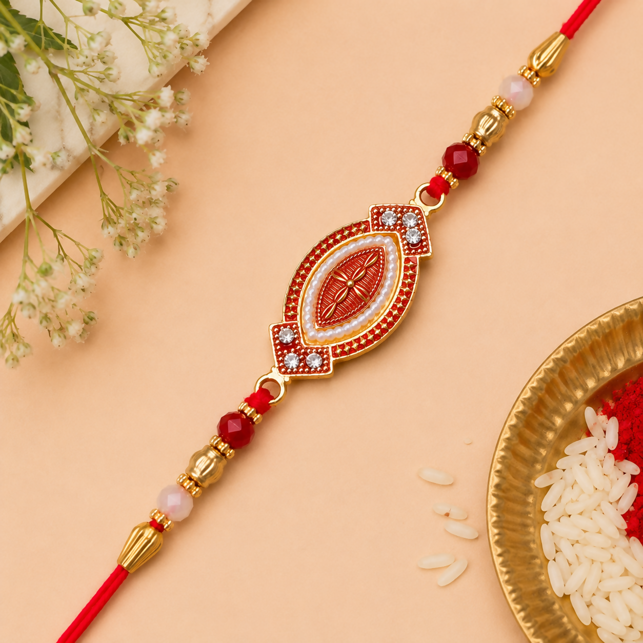 A red and gold bracelet with an oval centerpiece, adorned with white beads and red stones, lies on a light peach background