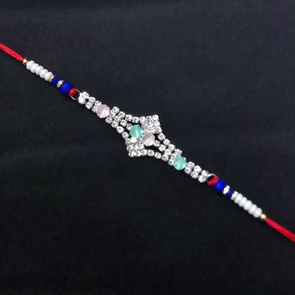 A red thread bracelet with a silver-toned, crystal-studded centerpiece and pink and green oval stones is displayed on a