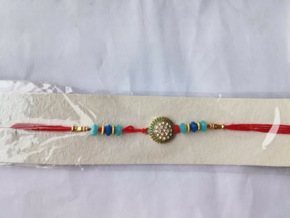 The red thread bracelet with its crystal-studded medallion and blue beads is packaged on a white card inside a clear plastic