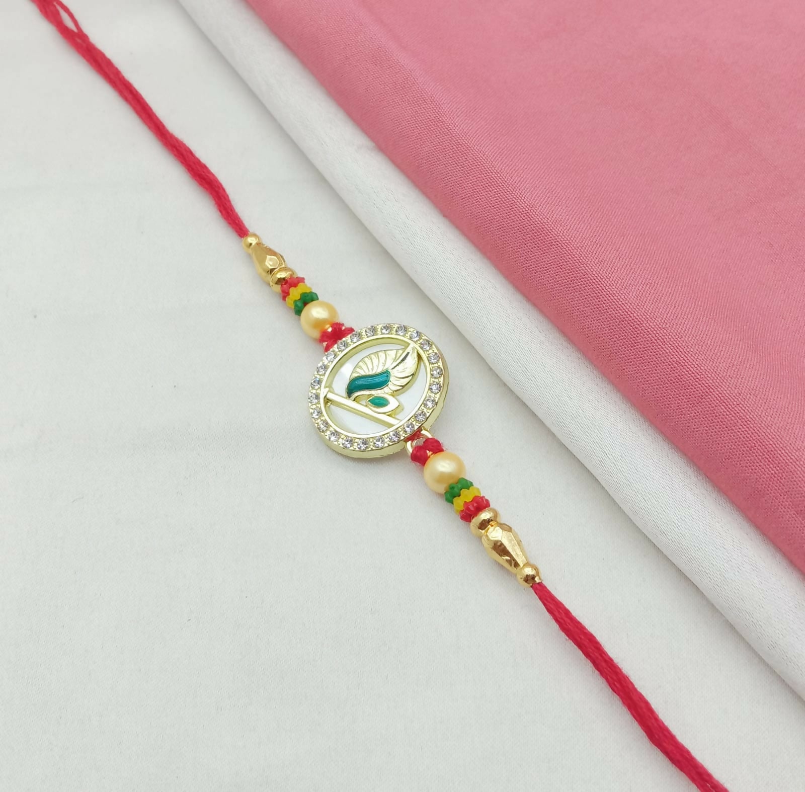 A golden Mor Pankh design with American diamonds and pearls on a red thread, against a simple pink and white fabric
