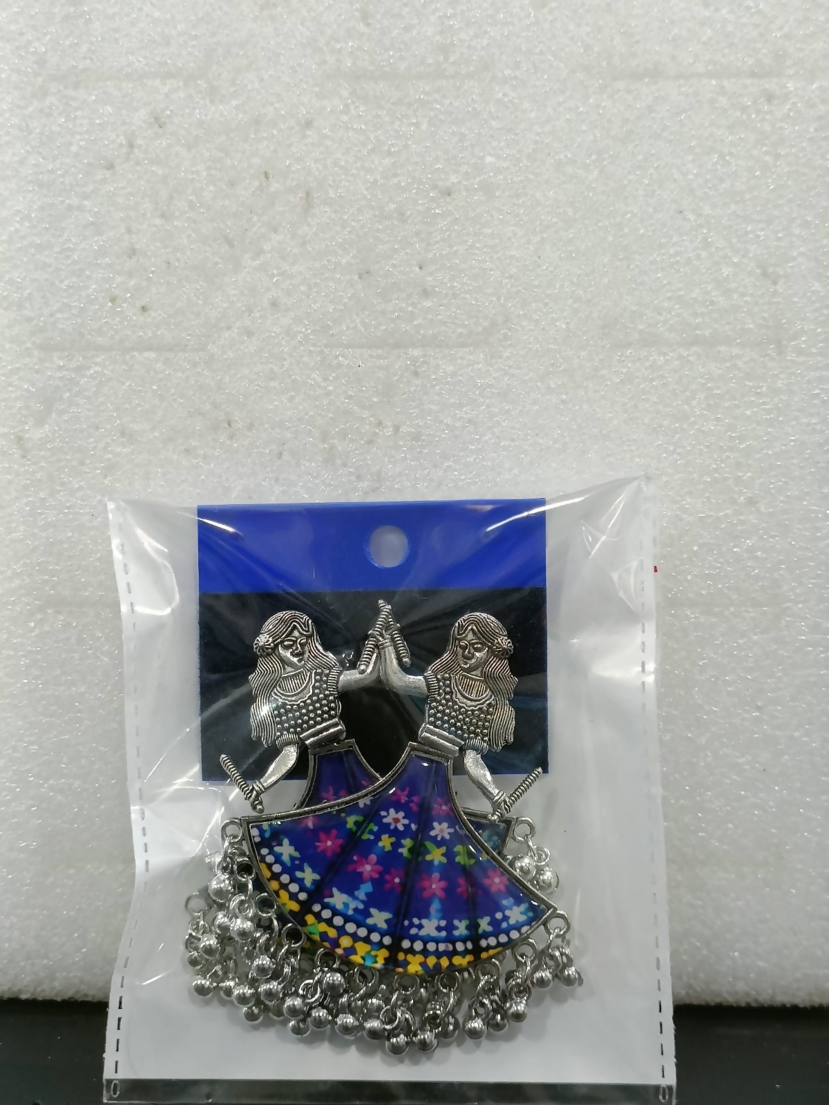 Pair of oxidized silver dancing doll earrings with blue floral skirts in clear plastic packaging.