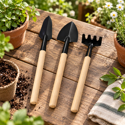 Three miniature gardening tools with wooden handles rest on a rustic wooden table surrounded by potted plants.