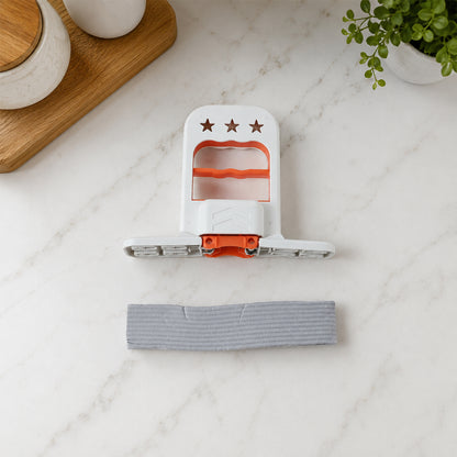 The white and orange mini mop is disassembled on a white marble countertop, with the gray sponge separate.