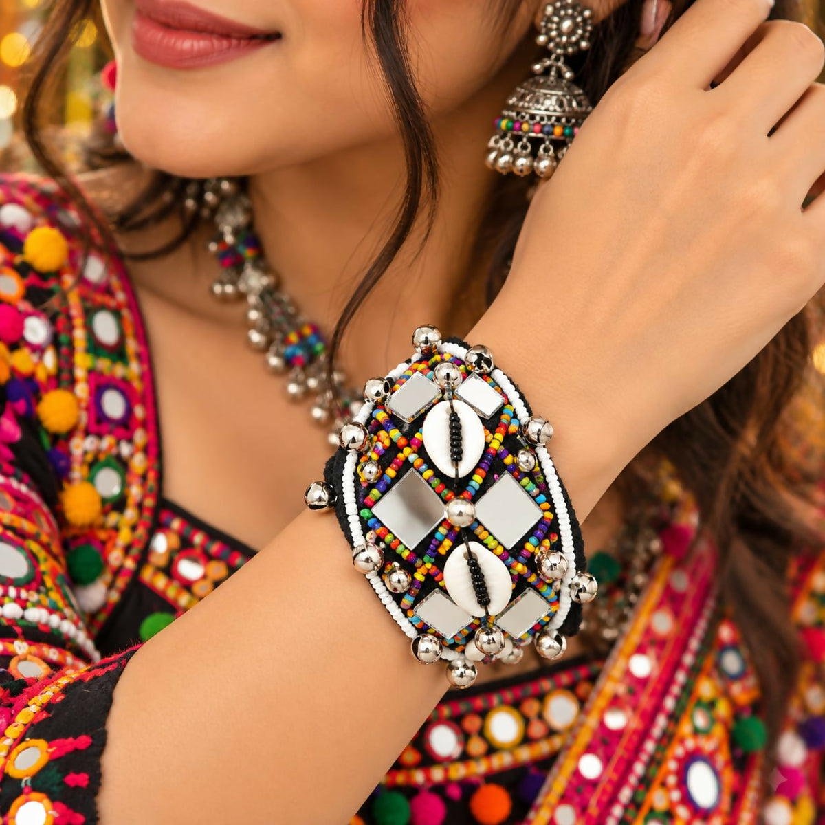 A woman's arm wears a wide black cuff bracelet with colorful beads, mirrors, shells, and silver bells.