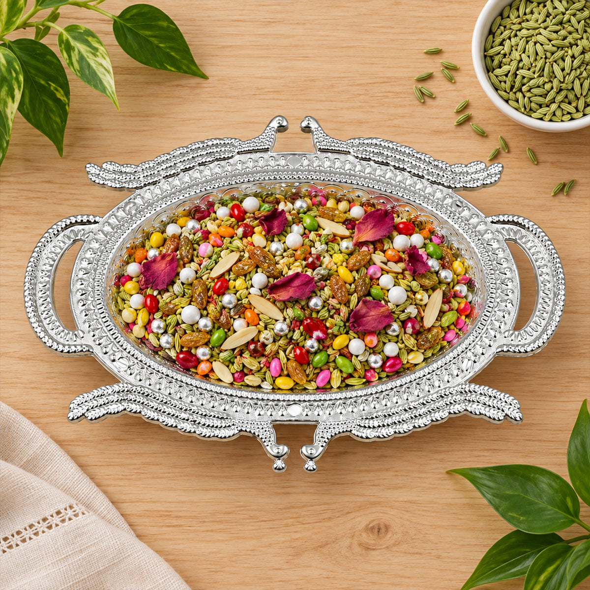 Ornate silver-colored serving tray filled with colorful mukhwas, nuts, and rose petals on a wooden surface.