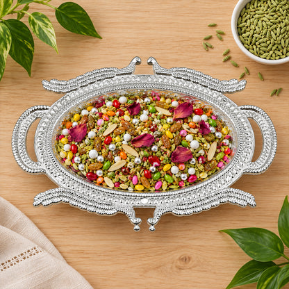 Ornate silver-colored serving tray filled with colorful mukhwas, nuts, and rose petals on a wooden surface.