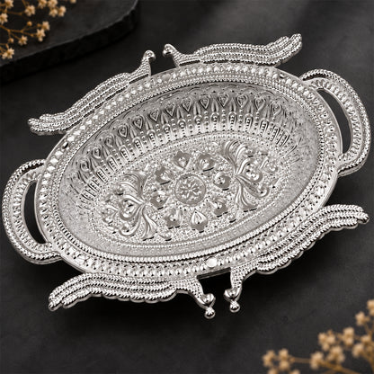 Empty silver-colored ornate serving tray with detailed patterns on a dark background with blurred floral elements.