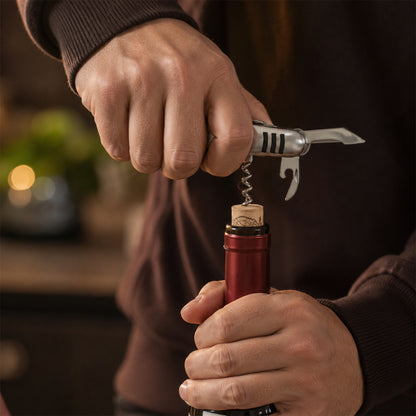 A hand uses the silver multi-tool's screwdriver to tighten a bolt on a bicycle fender.