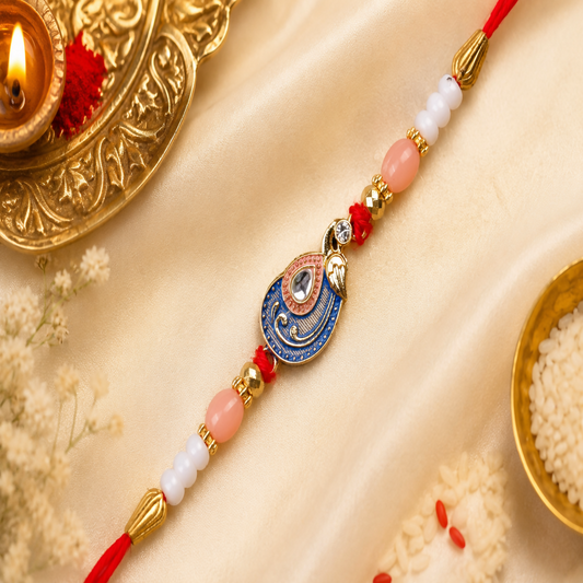 A red, blue, and gold peacock charm bracelet with pink and white beads lies on a gold satin cloth, next to a lit diya and