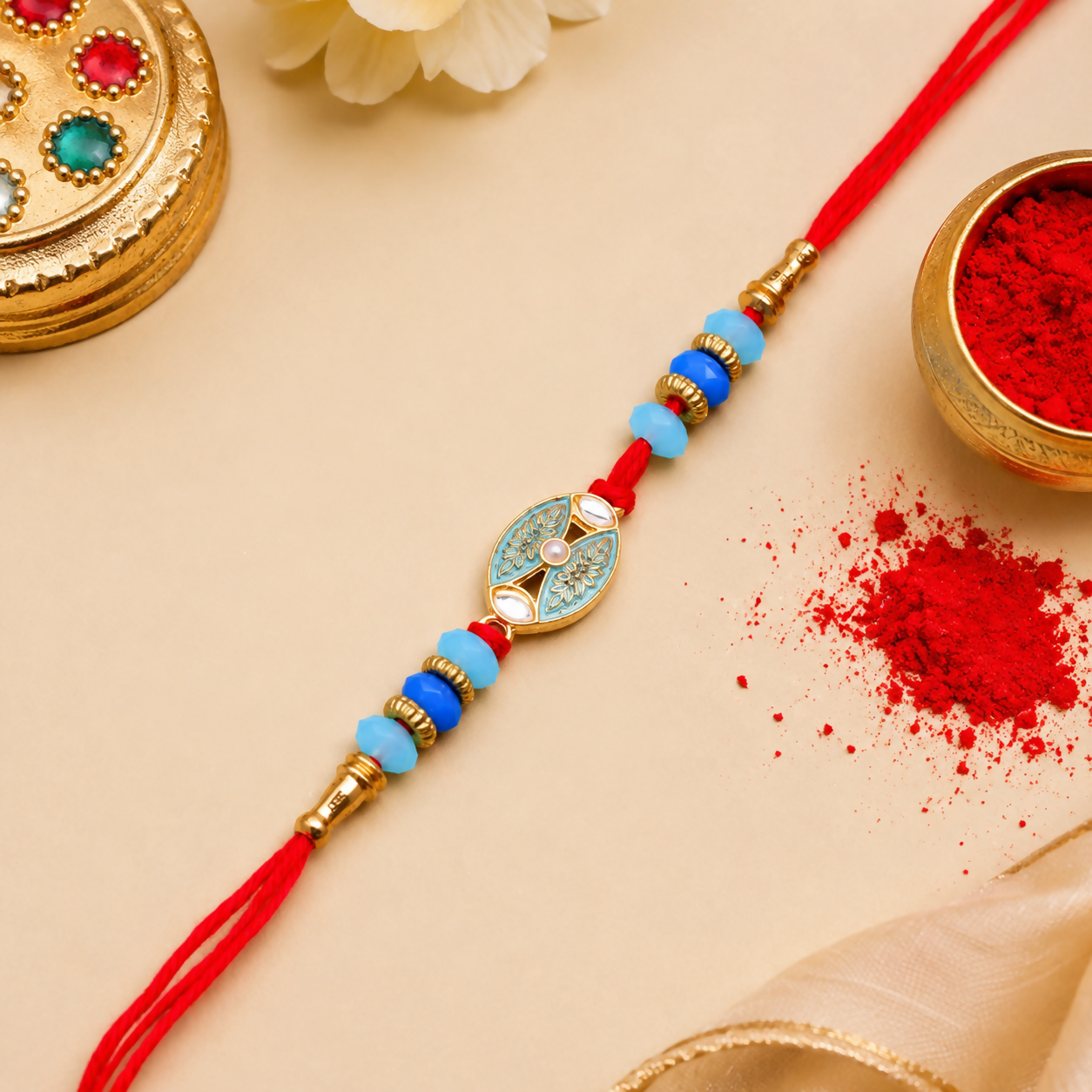 A red thread with blue and light blue beads, and a central golden oval charm with a light blue design, rests on a beige