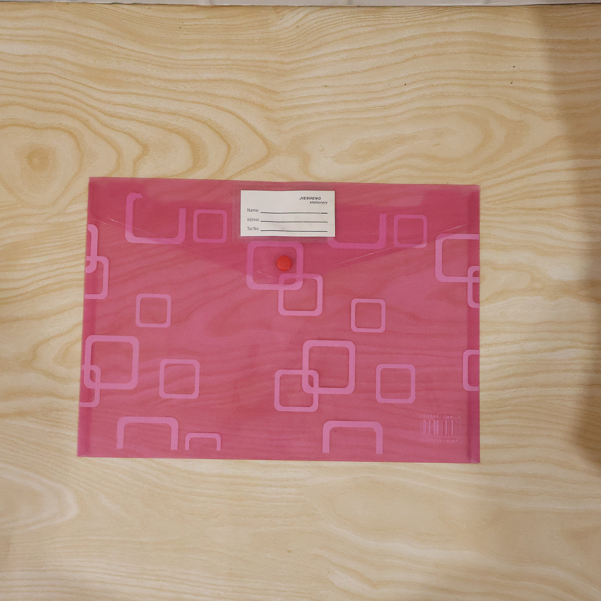 A pink plastic document folder with a button closure and a white label, centered on a light wooden surface.