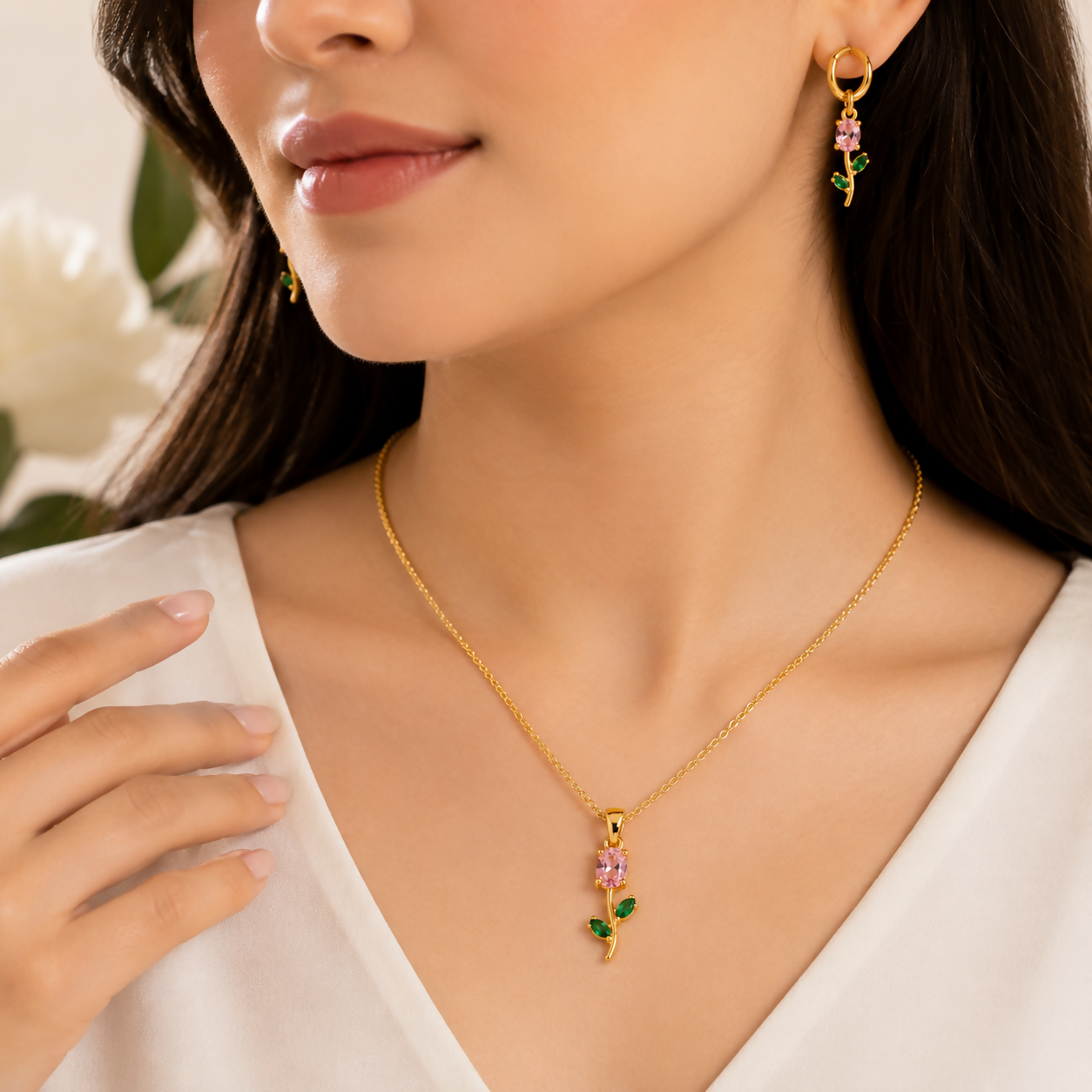 Detailed shot of the gold-plated earrings with pink crystals and green leaf accents.