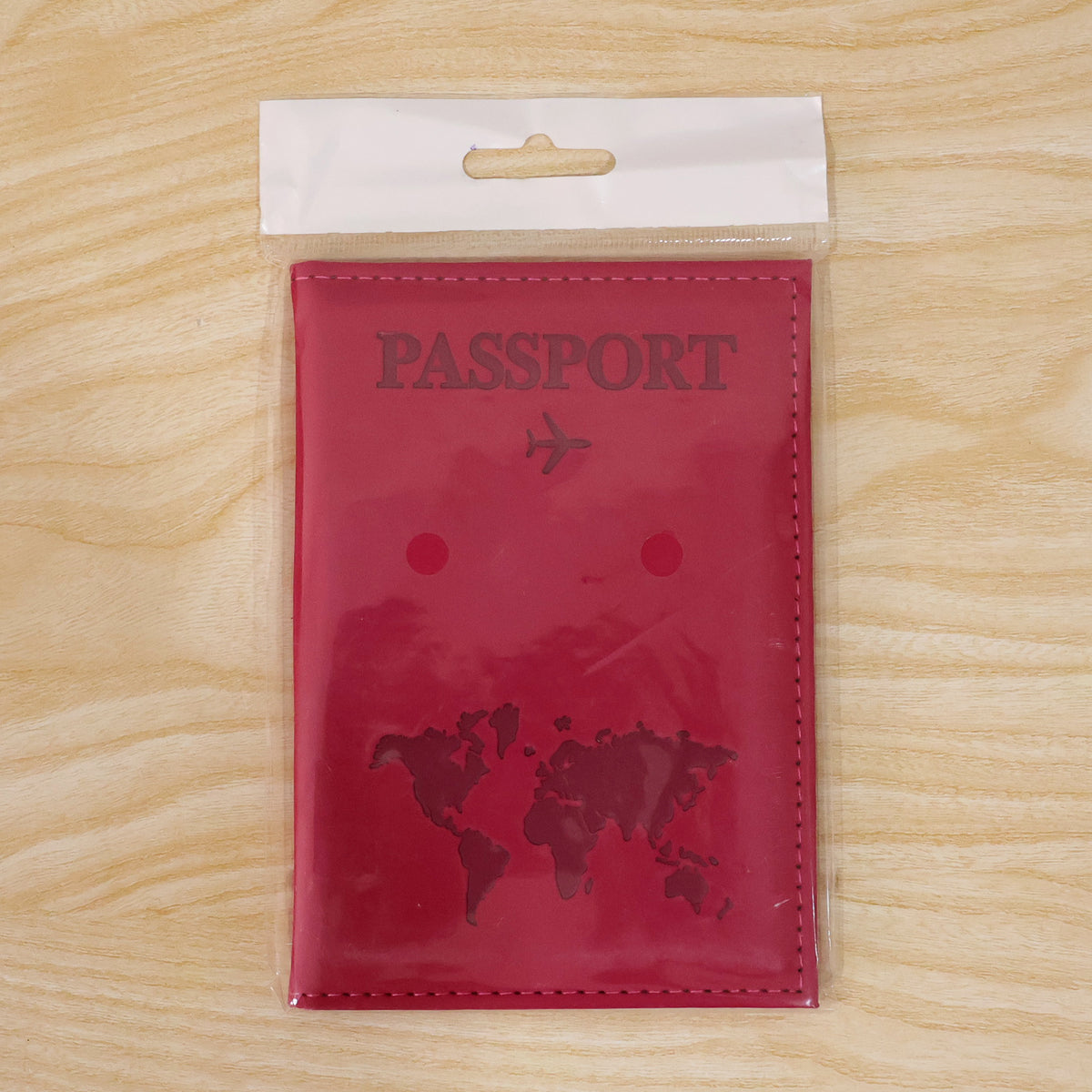 Pink passport holder with an embossed world map, sealed in clear plastic packaging with a white hanger.