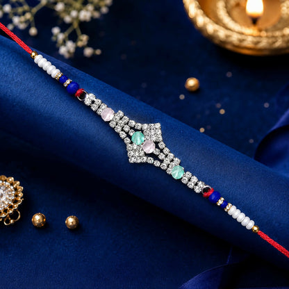 A red thread bracelet with a silver-toned, crystal-studded centerpiece featuring pink and green oval stones rests on a blue