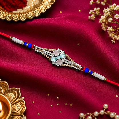 A red thread bracelet with a central diamond-studded floral design featuring pink and blue-green crystals, on a red silk