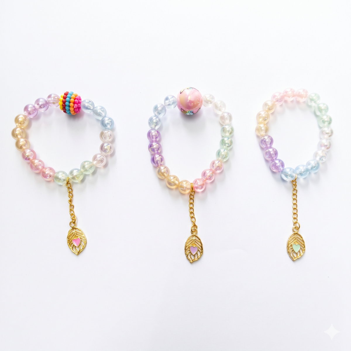 Three pastel beaded bracelets with gold leaf charms, each featuring a distinct central bead, arranged on a white background.