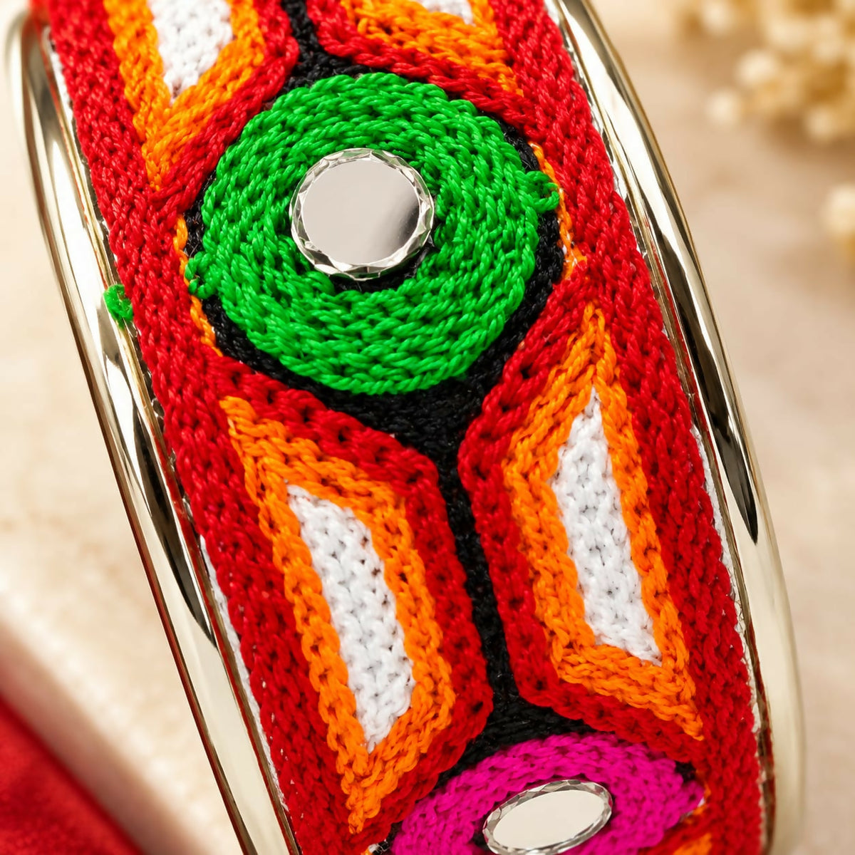 A close-up of the red, orange, white, and green embroidered cuff bracelet, highlighting the mirror details and threadwork.