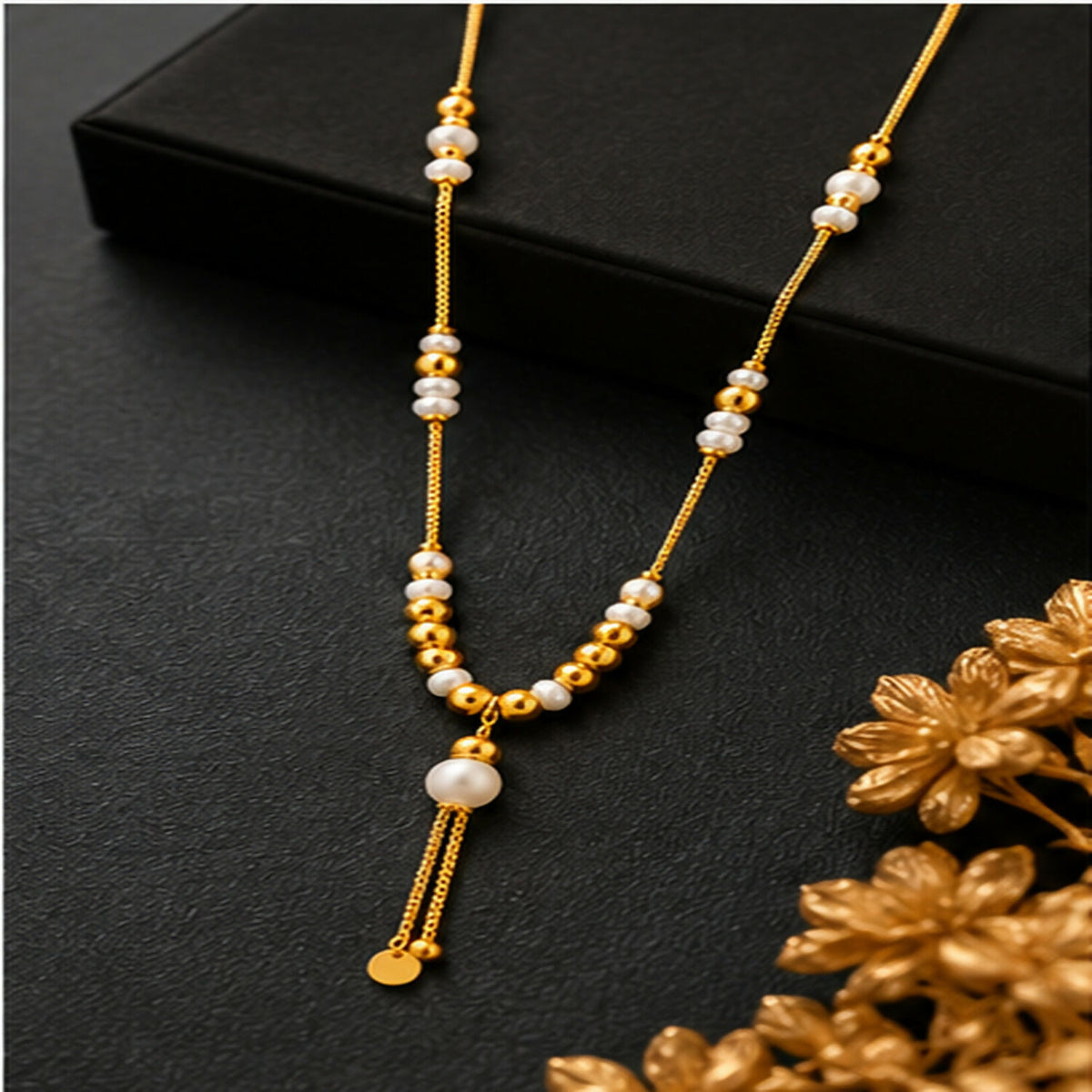 A gold tone necklace with white pearls and small gold beads on a black surface with golden floral decorations.