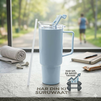 A light blue insulated tumbler with a handle and straw sits on a counter, with a blurred outdoor background.