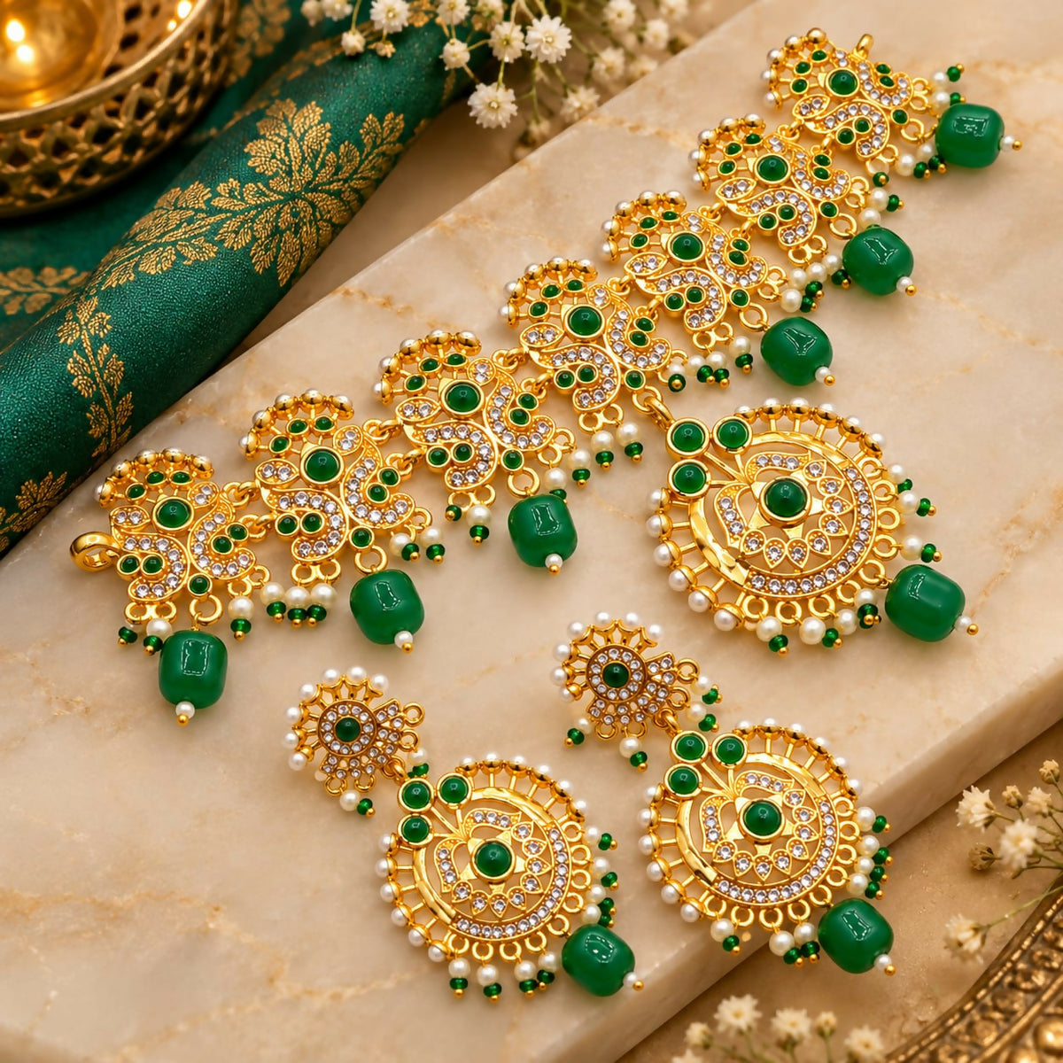 A gold-plated necklace and matching earrings with green beads and white stones, arranged on a marble surface.