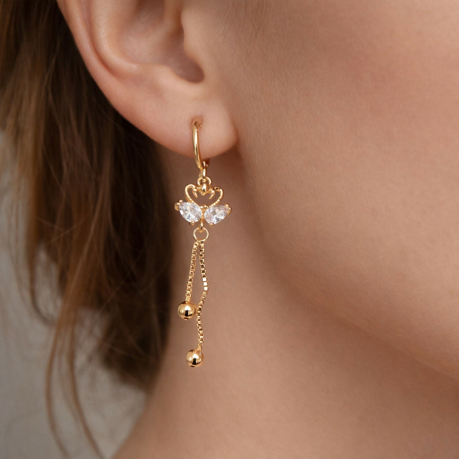 Close-up of golden swan motif earrings featuring crystal accents and gold chains