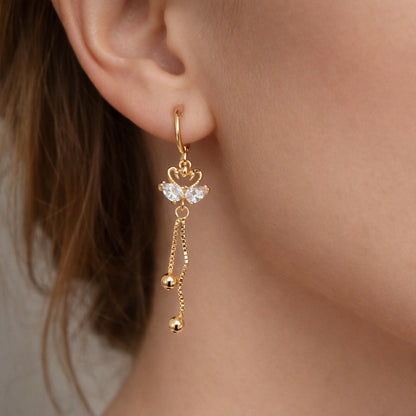 Close-up of golden swan motif earrings featuring crystal accents and gold chains