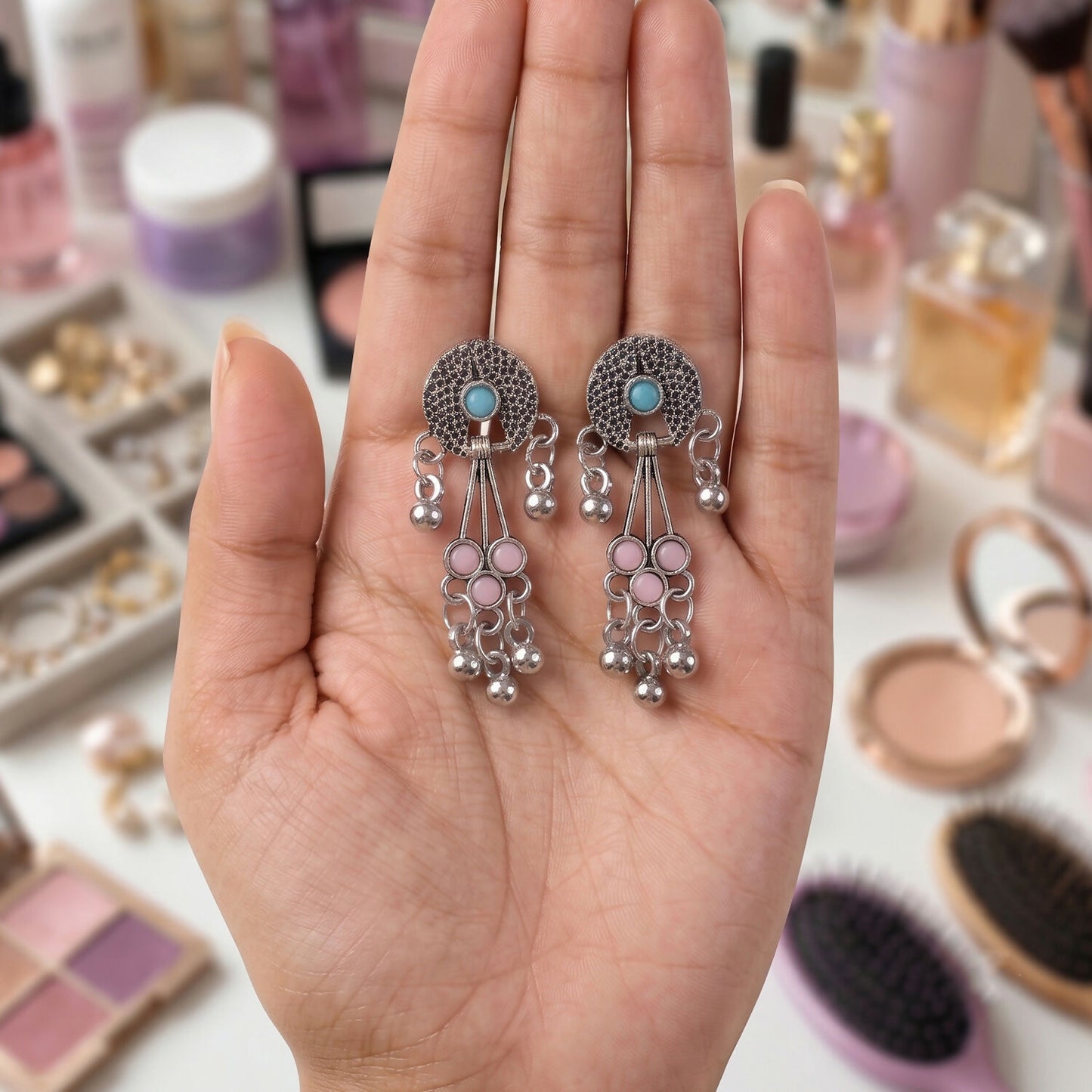 A hand holds the oxidised silver long drop earrings with pink and turquoise stones and ghungroo bells, surrounded by