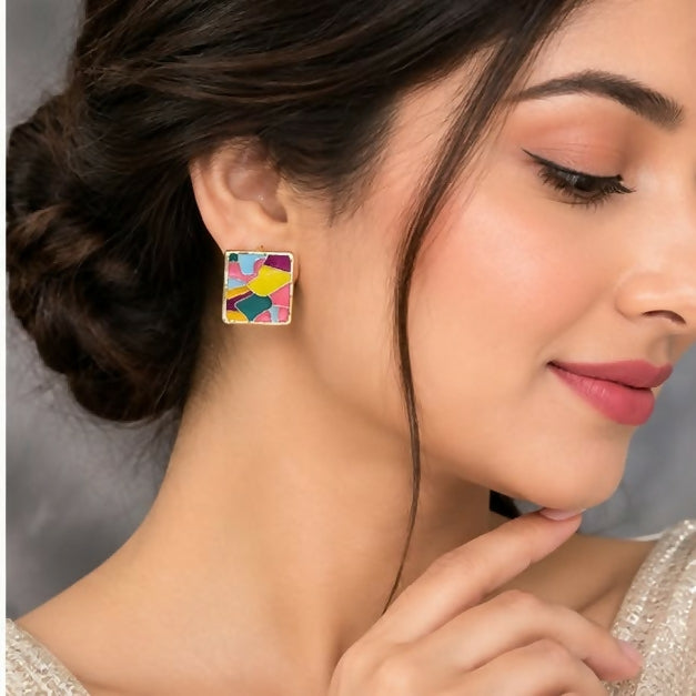 A woman models one multicolour enamel square stud earring on her earlobe, with her hair pulled back.