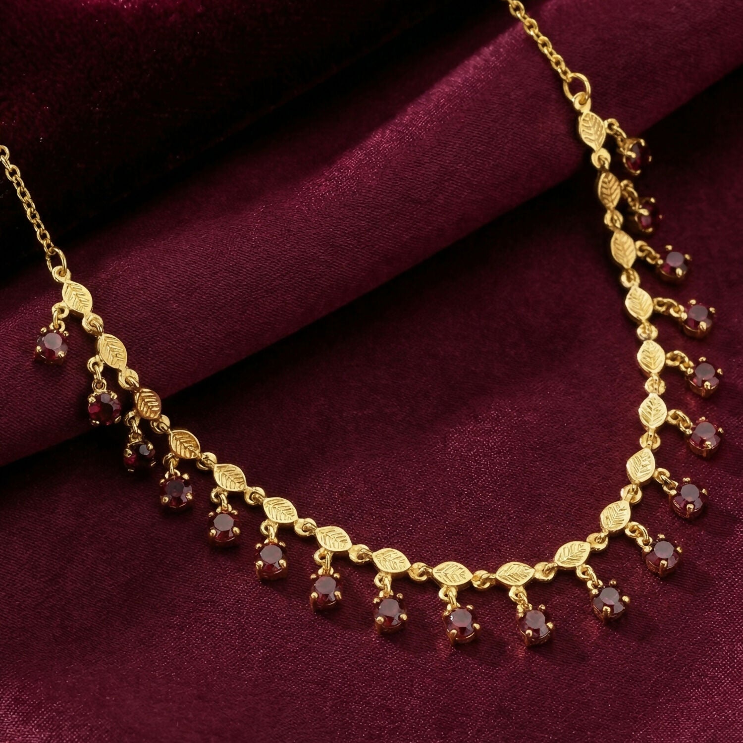 Close-up of intricate leaf pattern and red stones on gold plated necklace