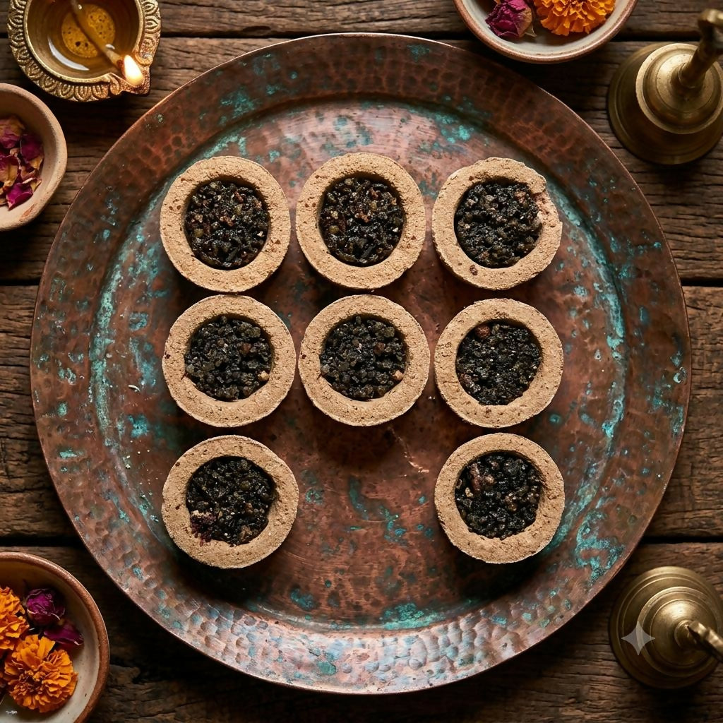 Nine round sambrani cups with dark contents arranged on a circular copper tray with floral accents.