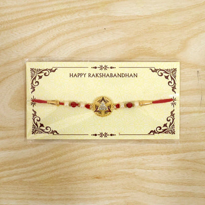 A gold-plated round centerpiece with a star design, red enamel, and clear stones, flanked by red and pearl beads on a red