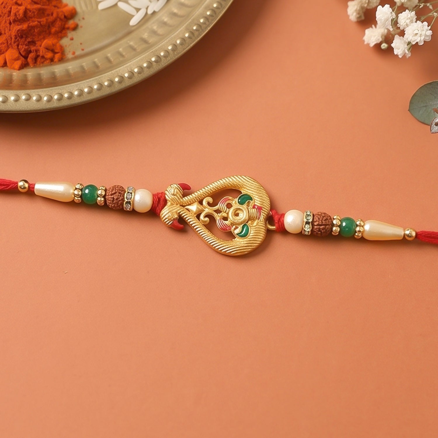 A red thread bracelet with a decorative gold-colored charm and white, green, and brown beads, resting on a light brown