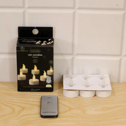 A black box of LED candles, six white LED candles in a tray, and a remote control on a wooden surface.