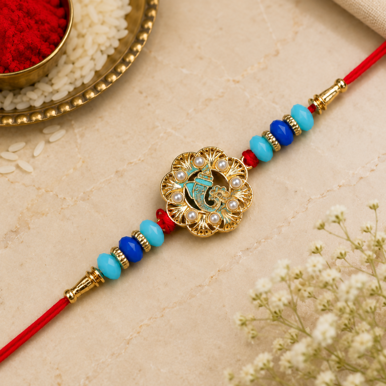 A close-up of the Ganesha charm shows intricate gold work, blue enamel, and tiny pearls, with blue and turquoise beads on a