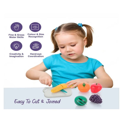 A young girl with pigtails cuts a yellow banana toy on a white board, surrounded by other colorful fruit toys.