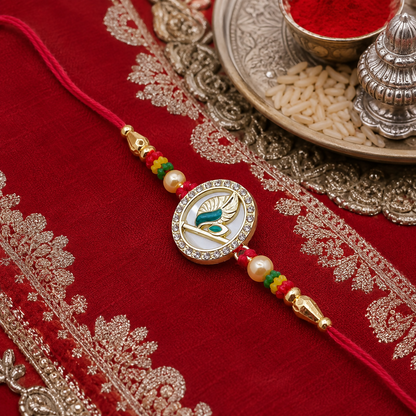 A gold-plated peacock feather design with American diamonds and pearls on a red thread, resting on a red embroidered cloth.