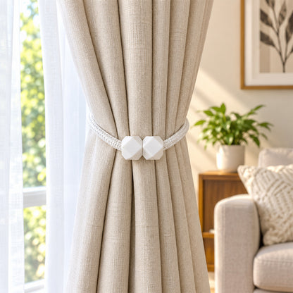 A beige curtain held back by a white braided rope tieback with geometric white plastic fasteners, in a bright room.