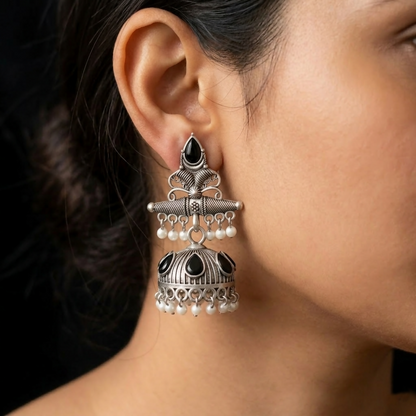 A woman models a single oxidized silver jhumka earring with black stones and white pearls, showcasing its size and dangle.