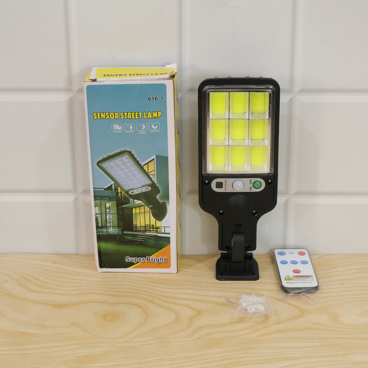 The black solar LED street light, its remote, and its product box are displayed on a wooden surface against a white tiled