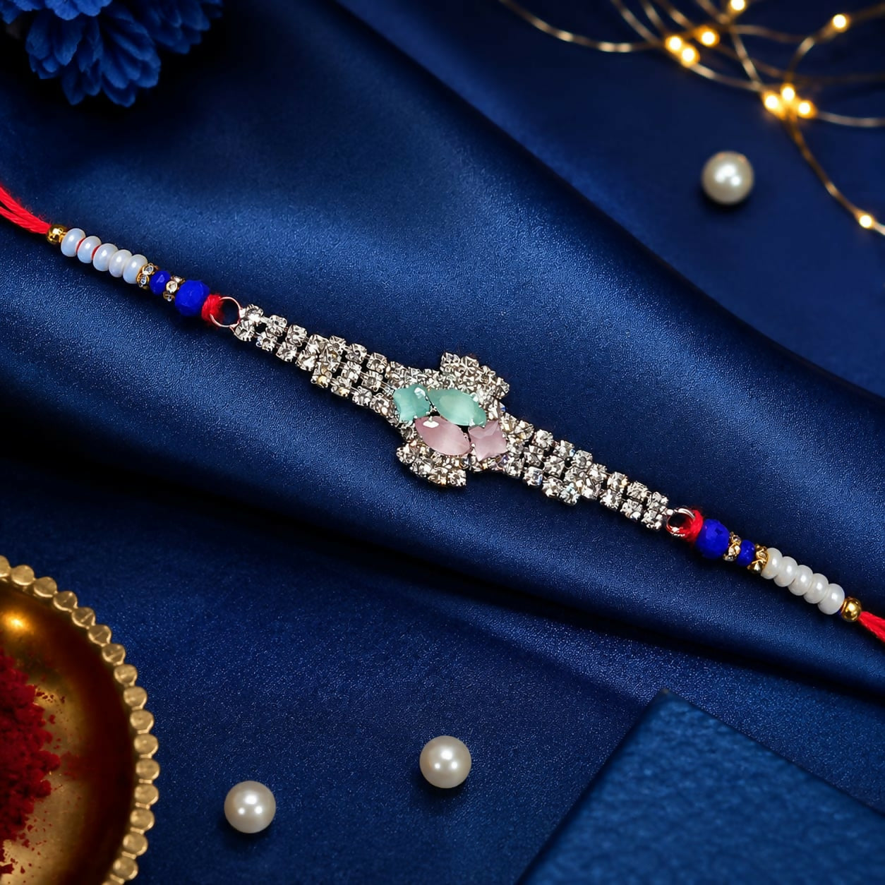 A beautiful crystal floral Rakhi with blue beads and red thread is presented on a vibrant blue satin background with