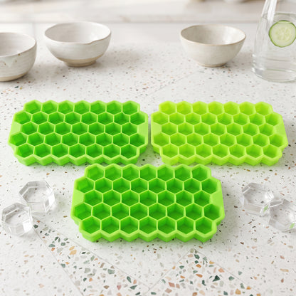 Three bright green silicone ice cube trays with hexagonal compartments sit on a speckled white surface, with two clear