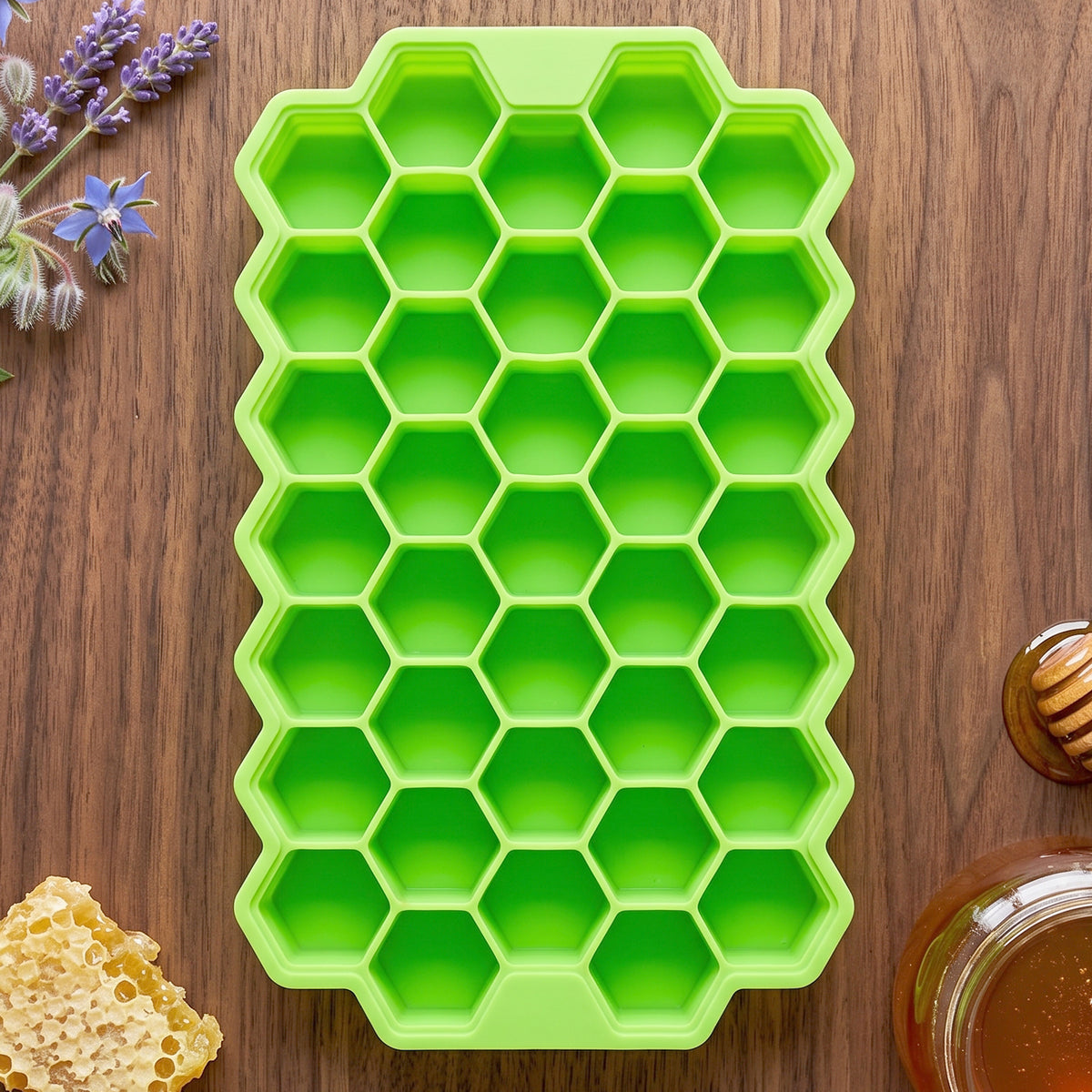 A single green silicone ice cube tray, with a honeycomb design, is centered on a wooden table next to lavender, honeycomb,