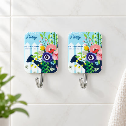 Close-up of two garden party themed adhesive hooks on a white tiled wall, featuring colorful floral designs.