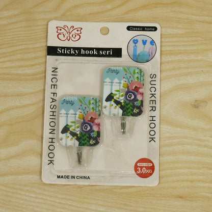 Two floral-patterned adhesive hooks in clear retail packaging on a light wooden surface, showing product branding.