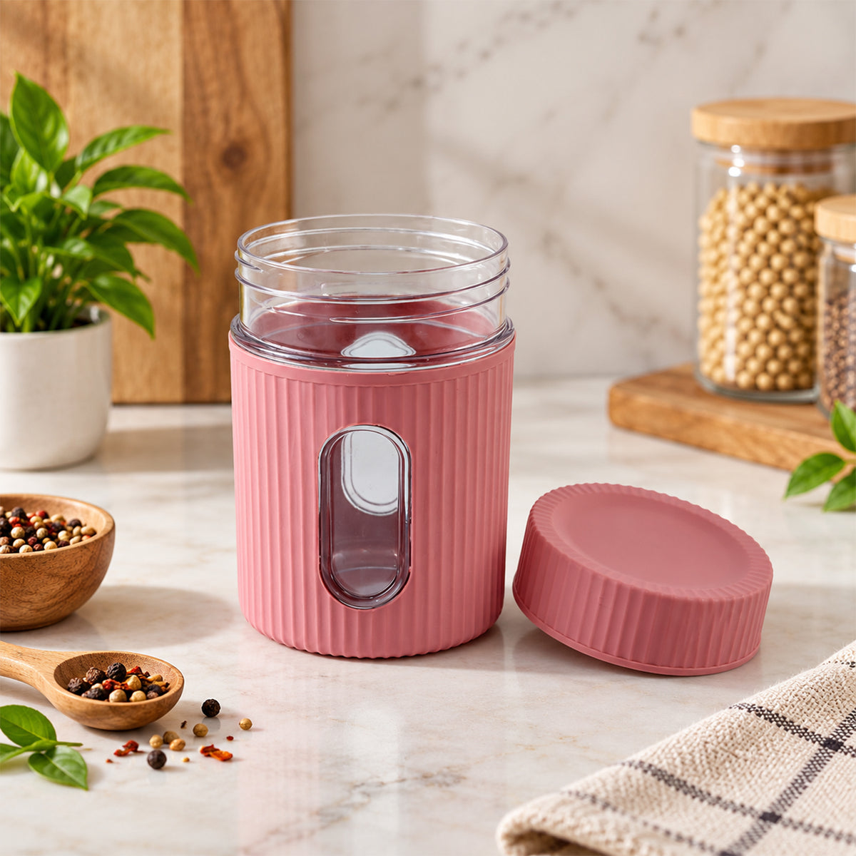 An empty pink ribbed storage jar with a clear window and its lid rests on a marble counter, with spices scattered nearby.